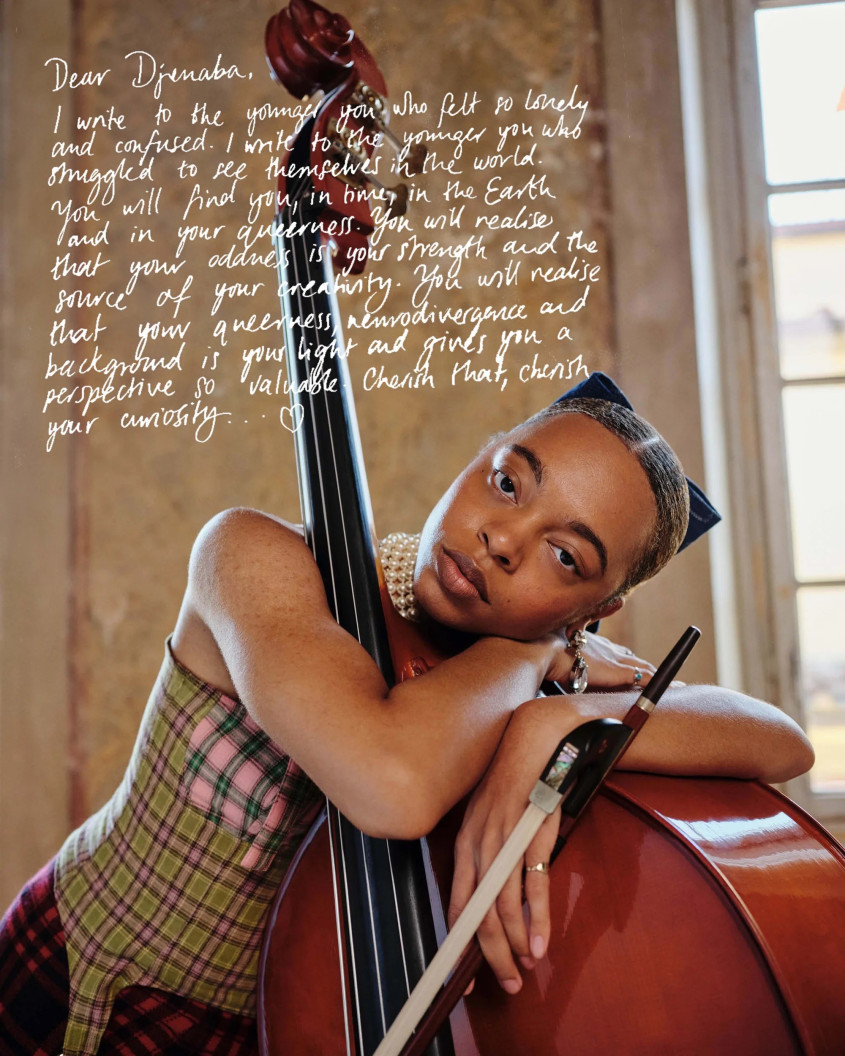 a Black woman hugging a double base in a patterned top, with a hand-written text covering part of the photo