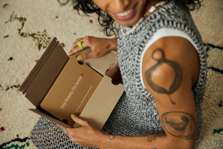 A customer unpacking a small cardboard box, on the box it says: Hey beauty I'm home