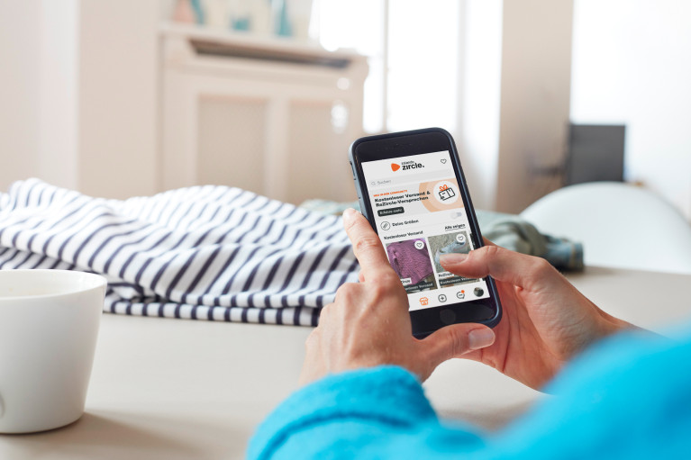Hands holding a smartphone in a home environment, Zircle app showing on the screen